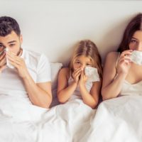 Parents and their daughter suffering from a cold wiping noses while lying on bed