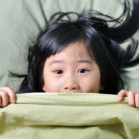 Scared little asian girl having childhood nightmares and hiding behind blanket