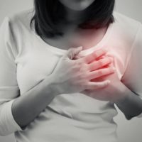 Woman is clutching her chest in acute pain caused by heart disease
