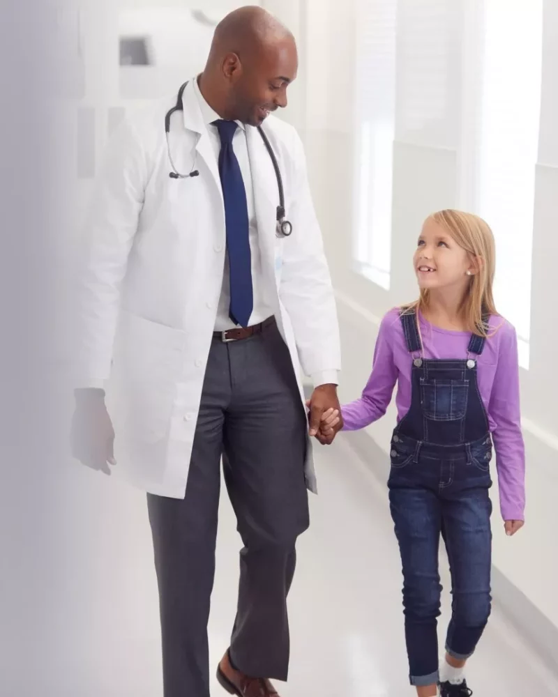 A doctor walking hand in hand with a young patient along the clinic corridor